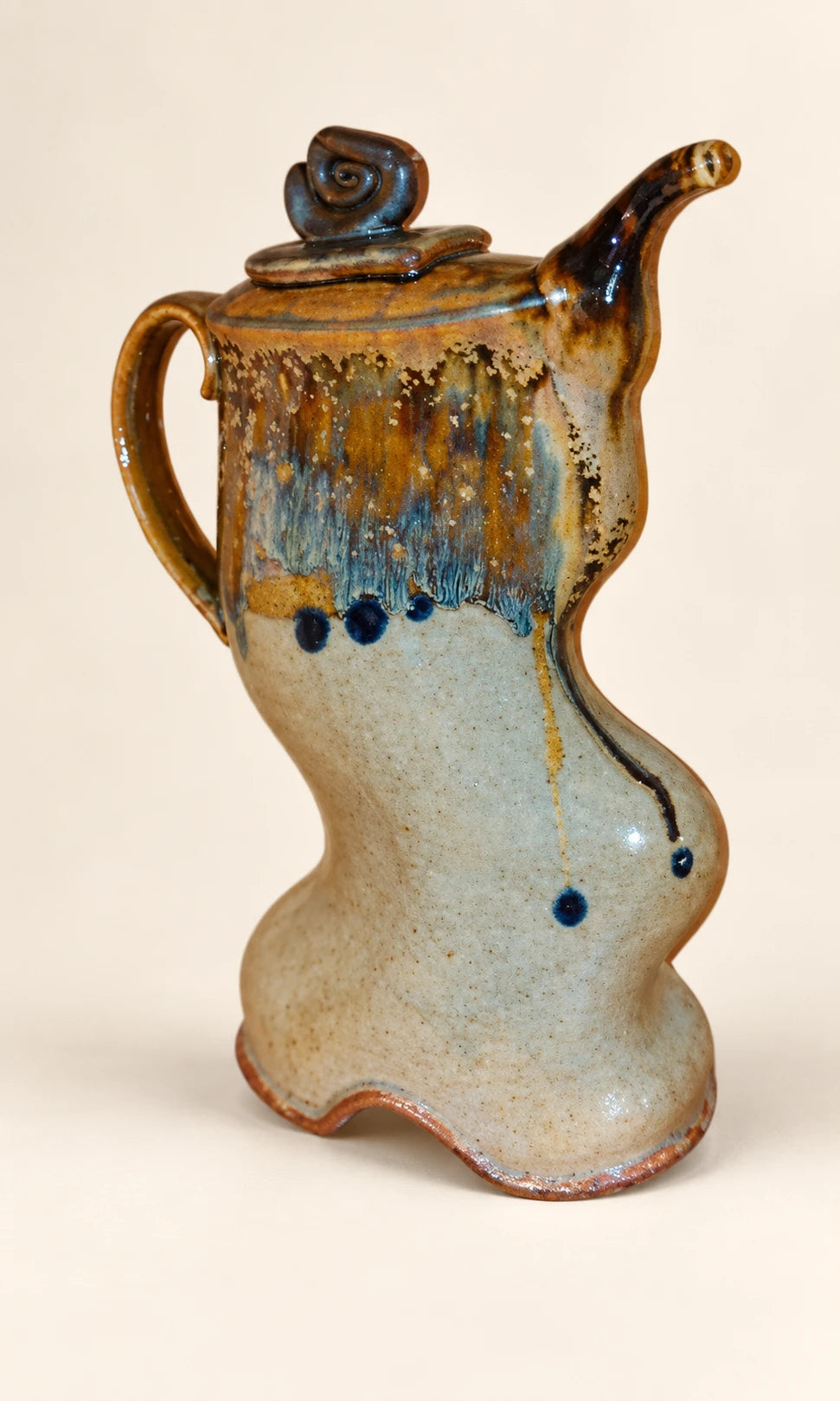 Sculptural teapot with a curled lid and flowing blue and amber glaze